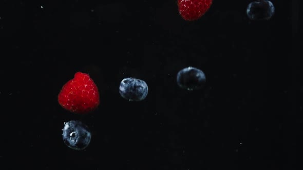 raspberry and blueberries falling in water slowmotion