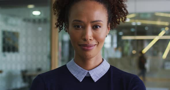 Portrait of smiling mixed race businesswoman in blue jumper standing in office