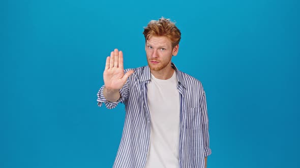 Serious Redhead Man Stretches Out Hand Showing Stop Gesture