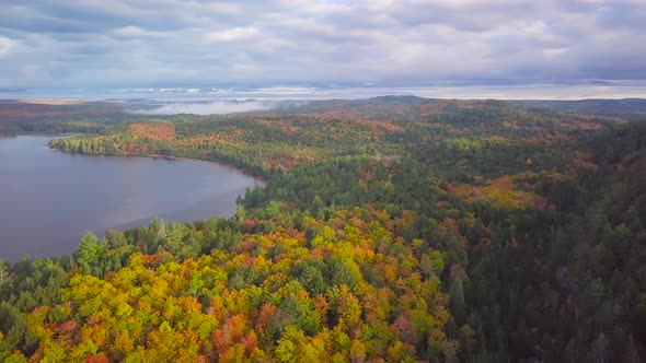 Aerial Daytime Wide Shot Flying Over Fall Forest Colors And Calm Misty Lakes Panning Right To Reveal