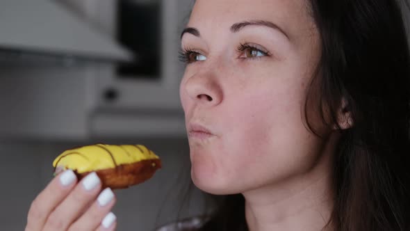 Young Brunette Woman Enjoys Eating a Sweet Bright Donut. Smiling Girl with Food Close-up.