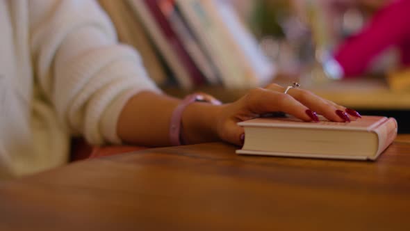 Happy Young Woman Speaks on the Phone in a Cafe Touches a Book with Her Hand