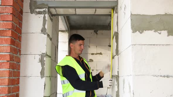 Construction worker at construction site measures the length of the window opening