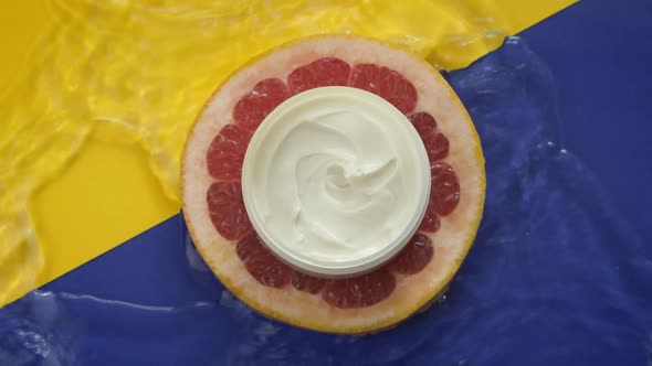 Jar with Moisturizing Cream on Piece of Fresh Grapefruit in Clean Water Splash