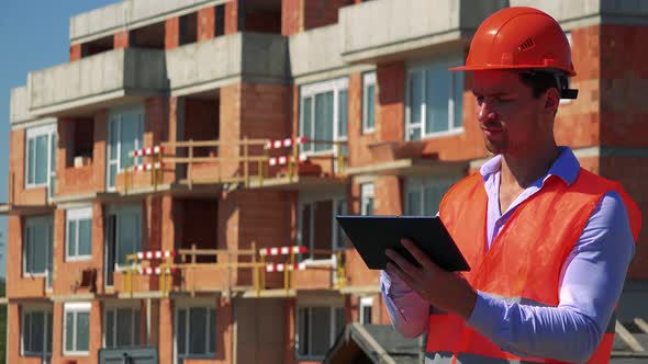 Construction Worker Works on the Tablet in Front of Building Site