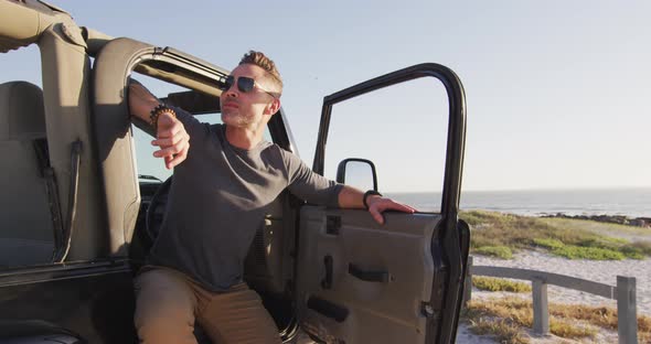 Happy caucasian man in sunglasses sitting in car with open door on sunny day at the beach