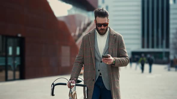 Young Man with Bicycle Holding a Smartphone Front of Building