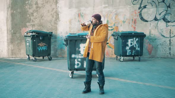 A Poor Man is Drinking Coffee Next to the Trash Bins