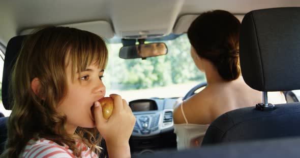 Girl having apple in the back seat of the car