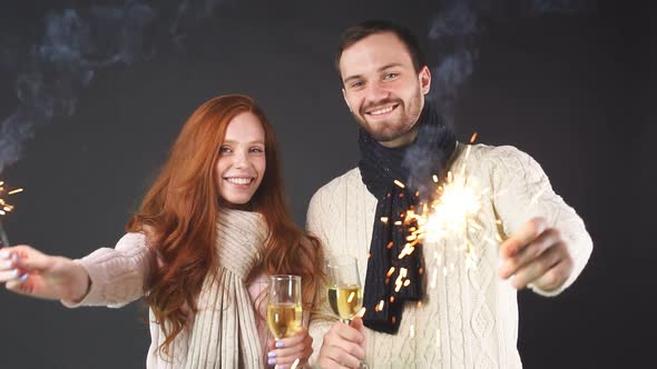 Studio Portrait of Couple with Champagne Glasses and Sparklers on Black Background