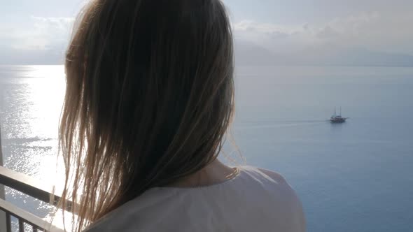 A Woman on a Balcony Talking To a Phone and a Sea View Behind Her