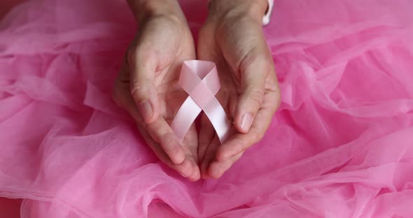 Pink Breast Cancer Awareness Ribbon in Hands on Pink Background