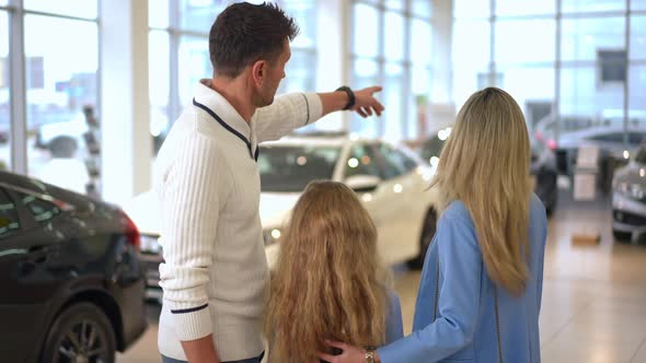 Back View Caucasian Man Woman and Girl Standing in Car Dealership Choosing New Automobile Talking