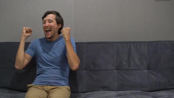 Young Man Sitting on a Couch Feeling Happy and Excited. Copy Space on a Right Side