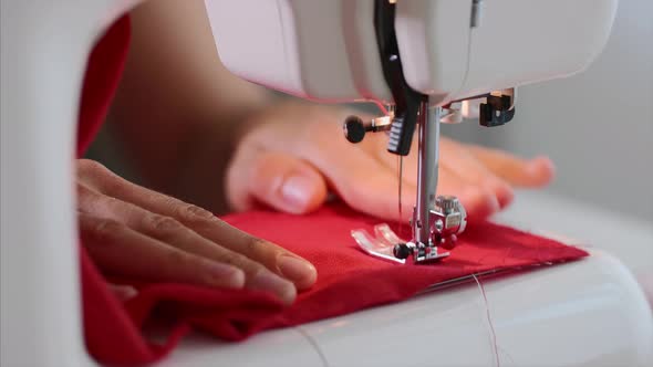 Hands of Woman Tailor Sewing Red Clothing on Sewing Machine with Straight Seam.