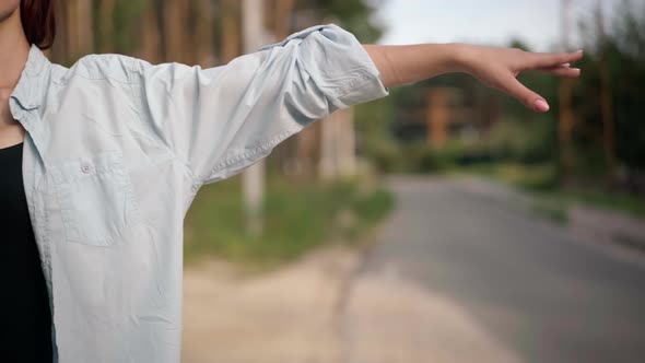 Unrecognizable Young Caucasian Woman Gesturing Hitchhiking on Suburban Road in Forest