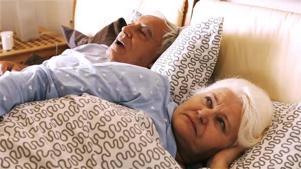 Man snoring and woman covering her ears while sleeping on bed