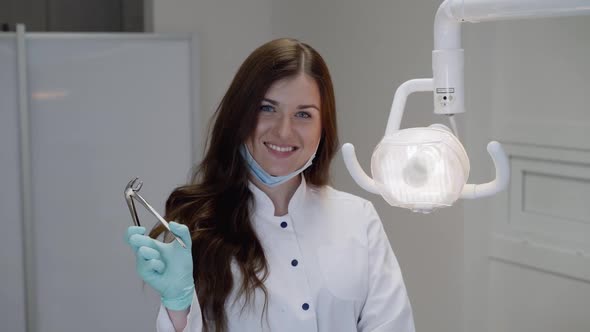 Female Dentist in Uniform Holds Dental Tool and Smiles at Camera in Clinic