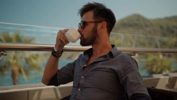 Businessman In Sunglasses. Businessman Drinking Tea On Vocation Resort. Man Sitting On Cafe At Sea.