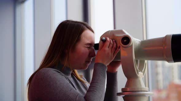 Young woman looks through stationary binoculars