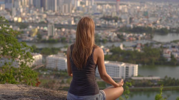 A Young Woman Meditates on a Mountain Over a Big City. Concept of Inner Peace in a Big City