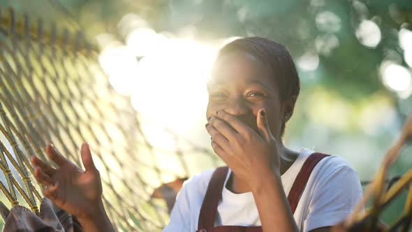 Cheerful African American Woman Laughing Looking at Camera Gesturing Sitting in Sunrays Outdoors