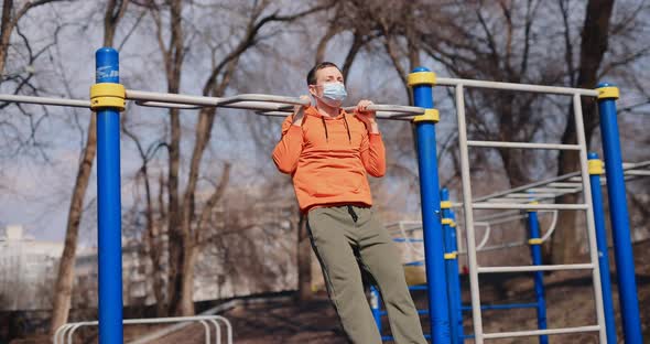 Man Pulls Up on the Bar Outdoor in a Surgical Mask