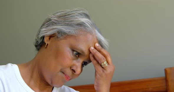 Side view of old black senior woman sitting on bed with hand on forehead in comfortable home 4k