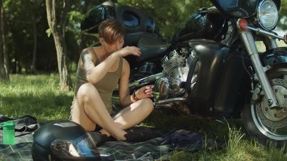 Female Biker Repairing Motorbike Engine in Park