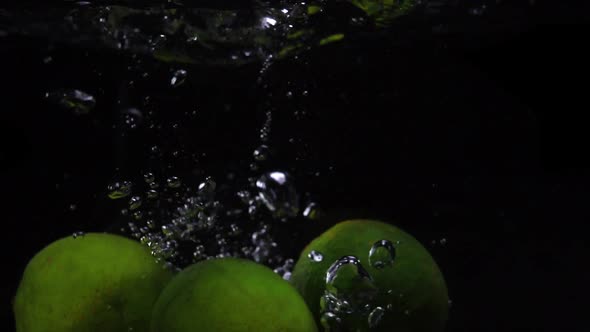 Three Green Lines Are Thrown Into a Container of Water. Video of Fruit in Slow Motion. Food Video.