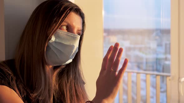 Young Caucasian Woman In Mask Looks Hopefully Out Window At Sunset