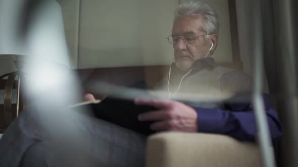 Portrait of an Elderly Grayhaired Man with Glasses Writing Down Thoughts in a Notebook Focused