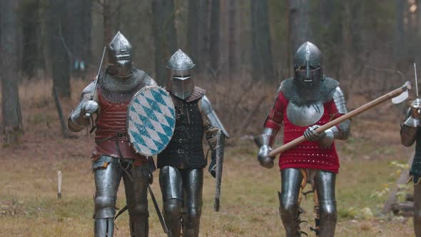 Four Men Knightes Walking in the Row in the Forest in Full Armour Holding Different Weapons