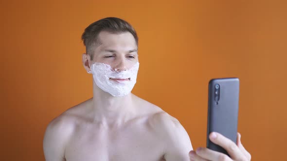 Cute Man with Shaving Foam on His Face Before Shaving His Stubble, He Makes a Video Call Using His