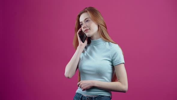 The Happy Freckled Young Woman Receives a Call and Speaks Enthusiastically on the Phone in a Pink