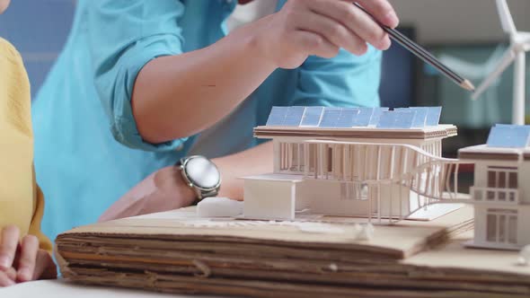 Close Up Of Man And Woman Helping Each Other Building The Model Of A Small House With Solar Panel