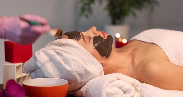 Cosmetologist Applies Rejuvenating Black Mask on Face of Woman in Spa