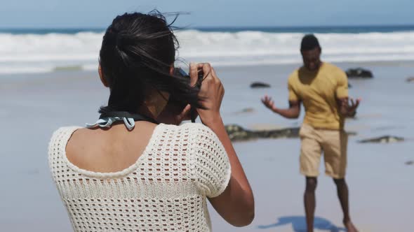 African american woman taking photo of her husband with digital camera at the beach