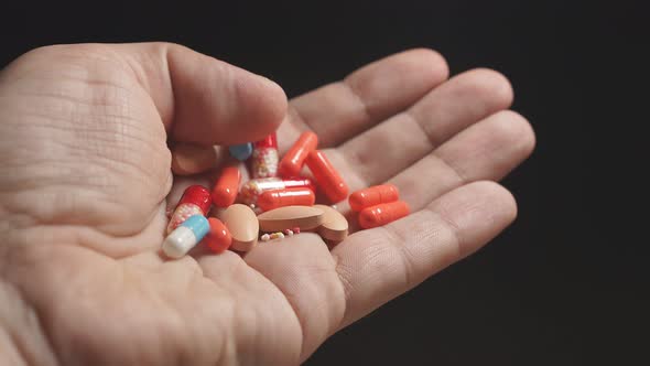 Close-up of a Man's Hand on a Dark Background Holding Many Different Tablets in the Palm