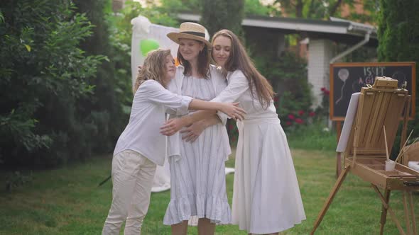 Caucasian Pregnant Woman Standing on Backyard As Young and Teenage Girls Hugging Expectant Smiling