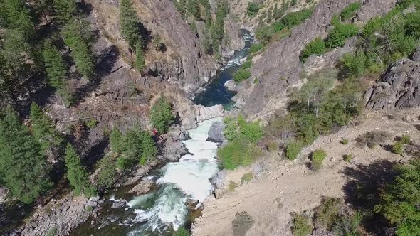 Aerial view of a river with white-water rapids and people walking their kayaks around the dangerous