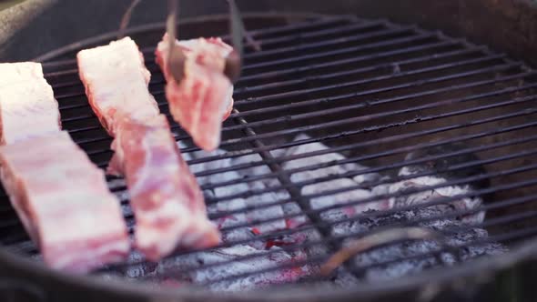 Slow Motion of Tongs Laying Meat on Smokey BBQ Grill