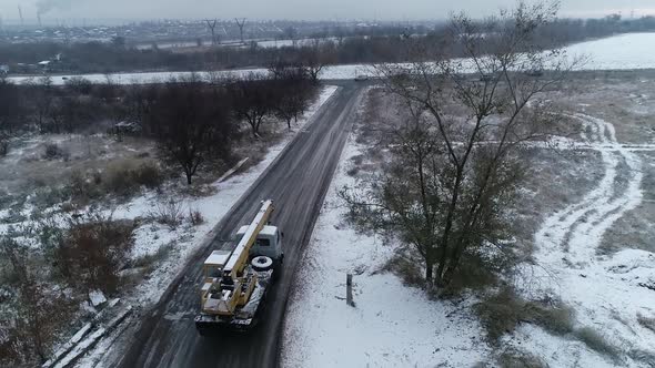 Aerial Footage of a Truck with a Crane on It Driving on a Road in Winter
