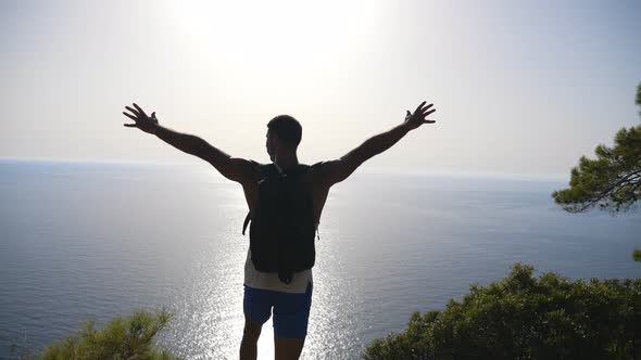 Male Hiker Standing on Peak and Victoriously Raising Hands Rejoicing Success. Young Man with