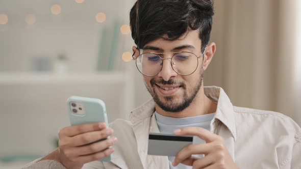 Closeup Bearded Arabic Business Man in Glasses with Credit Card and Phone Makes Purchase Online