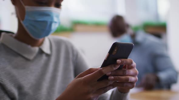 Diverse male and female business colleagues in face masks, woman using smartphone in office