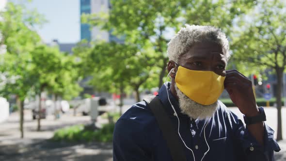 Close up of african american senior man in face mask wearing earphones on the road