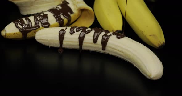 Pouring a Banana with Melted Dark Chocolate Syrup. Black Background