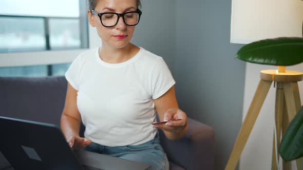 Woman with Glasses Sits on a Sofa in a Cozy Room and Makes an Online Shopping Using a Credit Card