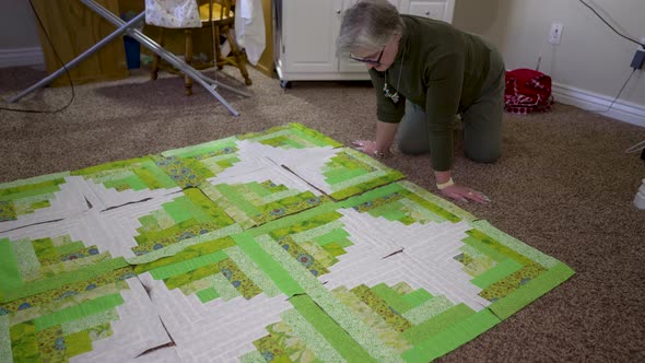 A senior Caucasian woman completes the final arrangement of her quilt blocks
